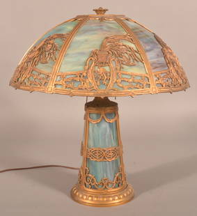 Early 20th Century Slag Glass Table Lamp.: Attributed to Edward Miller, Meridian, CT. Opaque, purple and blue slag glass with lighted base, gilt, spelter metal vase, bird, foliate and scroll designs. 22-1/2" H x 19-1/2" diam.
