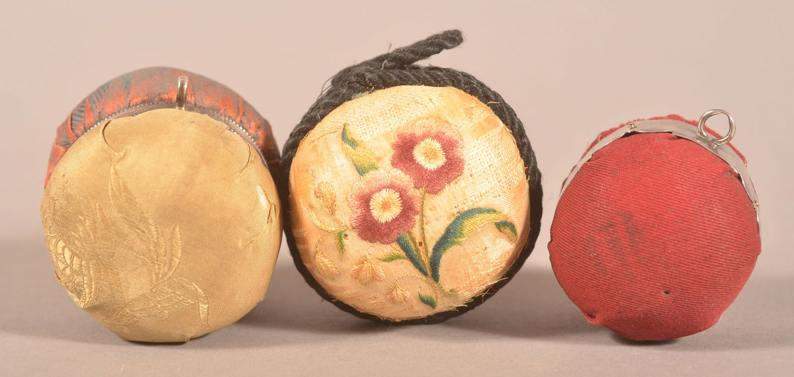 Three 19th Century Fabric Ball Pin Cushions.: Two with silver bands, one with silk floral embroidery. Largest, 2" x 2-1/2".