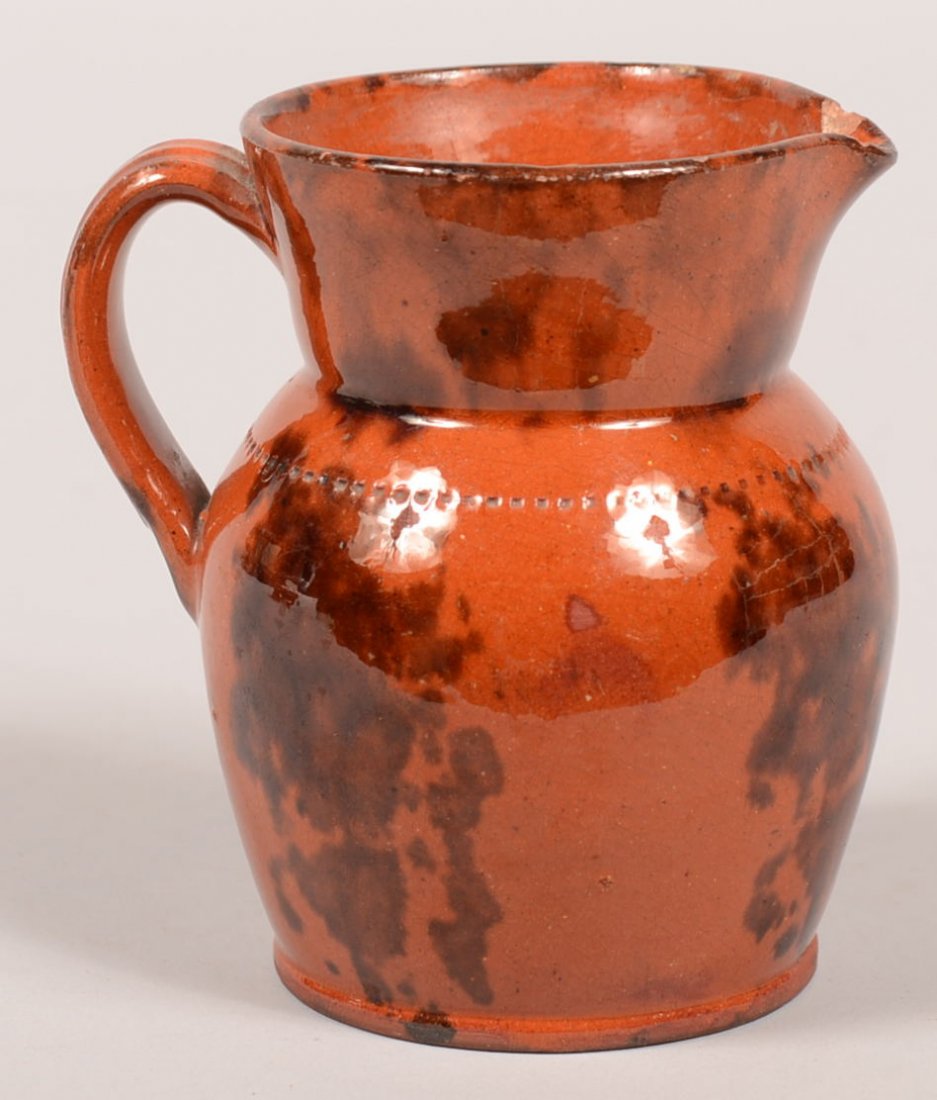 54. 19th Century Redware Pottery Cream Pitcher. Bulbous: 54. 19th Century Redware Pottery Cream Pitcher. Bulbous body with coggle wheel band, pinched spout, applied loop ribbed handle and molded base rim. Mottled manganese glaze on reddish orange glazed gro