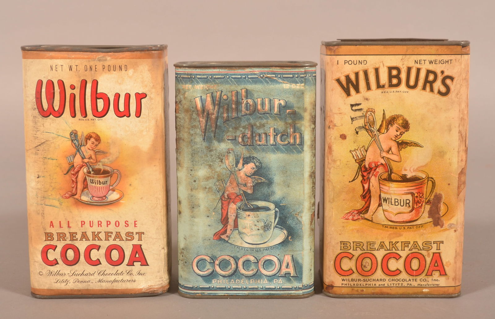 Three Wilbur's Cocoa Advertising Tins.: Difficult to find 1 lb. tin with blue paper label from Philadelphia, PA. Two other 1 lb. cardboard body tins from Lititz, PA. Provenance: James Hoffman Collection. Largest, 6-3/4"H x 3-3/4"W x 2-1/2"D