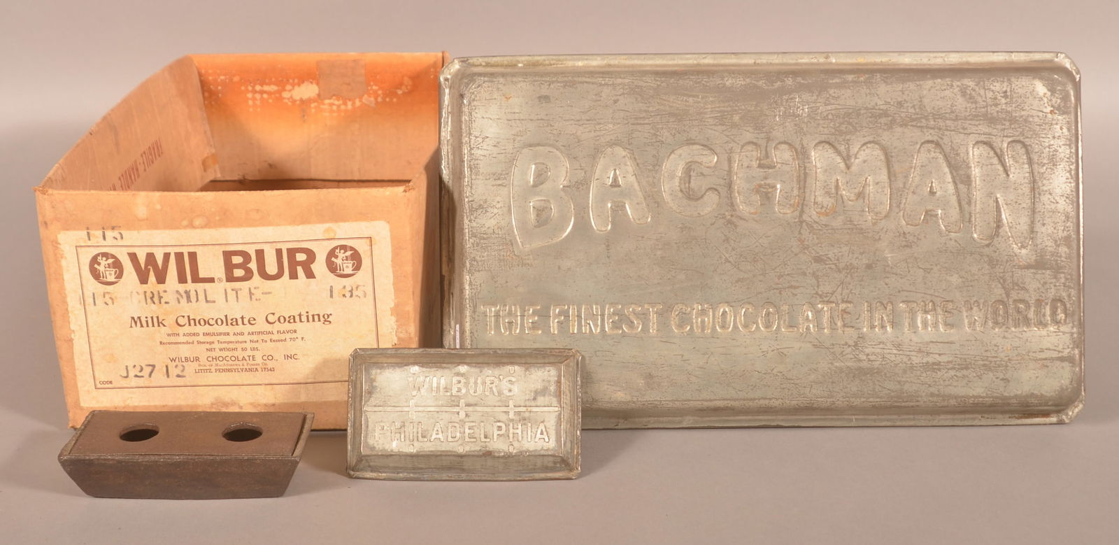 Wilbur's and Bachman Chocolate Advertising.: Bachman baking pan, small early Wilbur's baking pan from Philadelphia, cardboard Wilbur's shipping box, and a small cast iron primitive trough. Provenance: James Hoffman Collection. Bachman, 2-1/4"H x