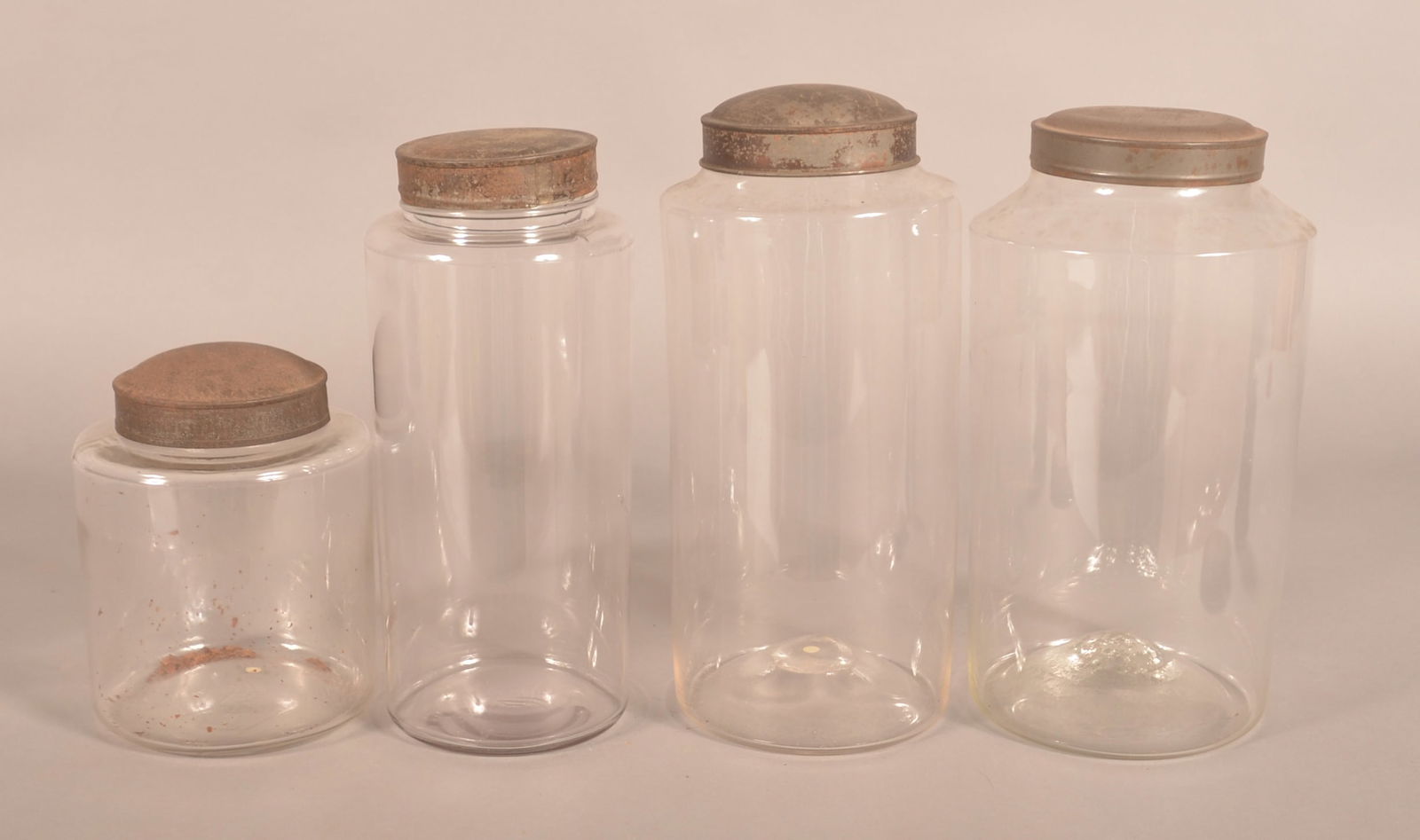 Four Early Graduated Glass Apothecary Jars.: Two largest are pontiled. 19th century. Original tin lids. One extra tin lid comes with the group. Largest, 12"H x 6"D