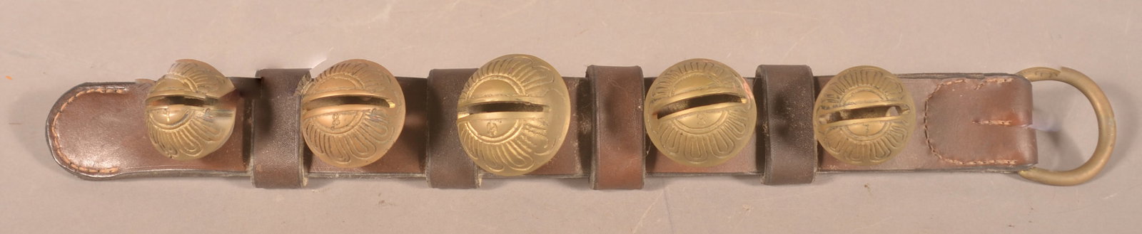 Small Leather Strap Brass Christmas Sleigh Bells: Small custom leather strap with 5 graduated brass bells. Each bell with embossed design and numbered 7, 8, 9. Bells are secured with cotter pins, an earlier design than rivets. Brass ring at end. 20"L