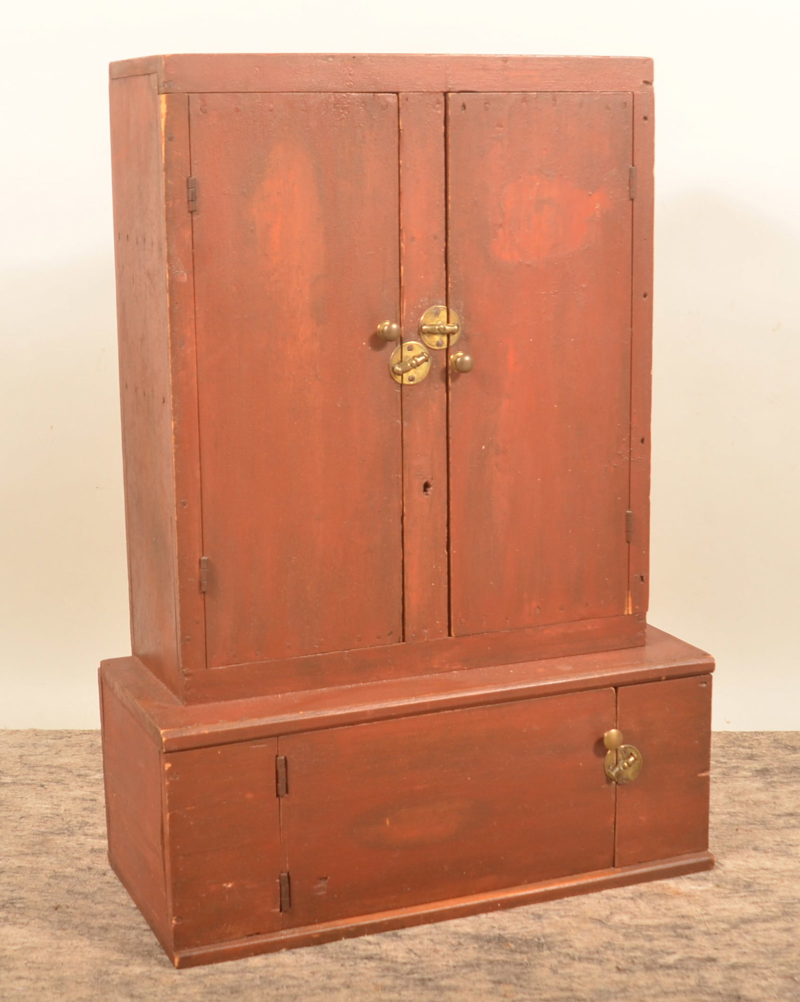 Tabletop 2-Door Over 1-Door Red Cupboard: Unusual form, two separate pieces that are nailed together. Top piece is pine with two interior shelves. Slab doors have two battens on each. Mix of square and round nail construction. Base is matchin