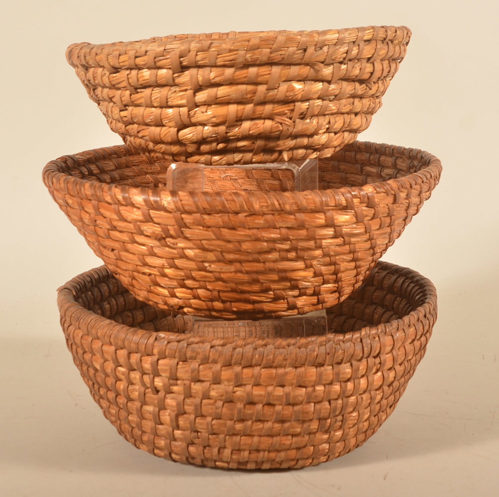 Group of Three Antique Rye Straw Baskets: Three different size Pennsylvania rye straw baskets in the traditional bowl form. Largest basket with an unusual added row of banding on half of the top row. Largest, 4 1/2"H x 12"D