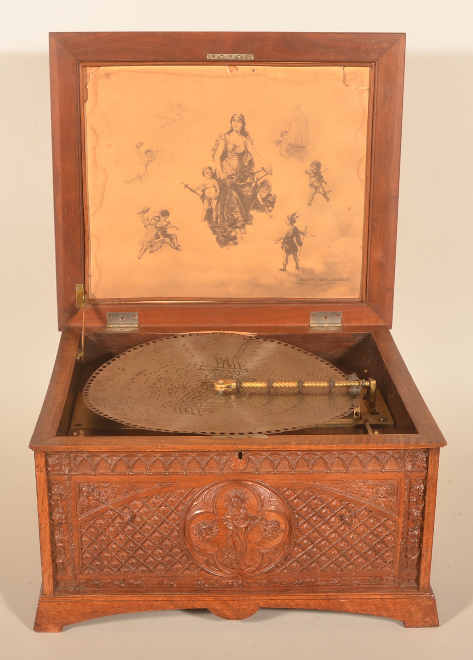 American Regina 15 1/2" Disc Music Box: Late-19th-century Regina double comb music box with a wonderful carved oak exterior featuring cherubs, quatrefoil medallions and Regina's maiden in the center. Interior of lid with heavy paper lithogr