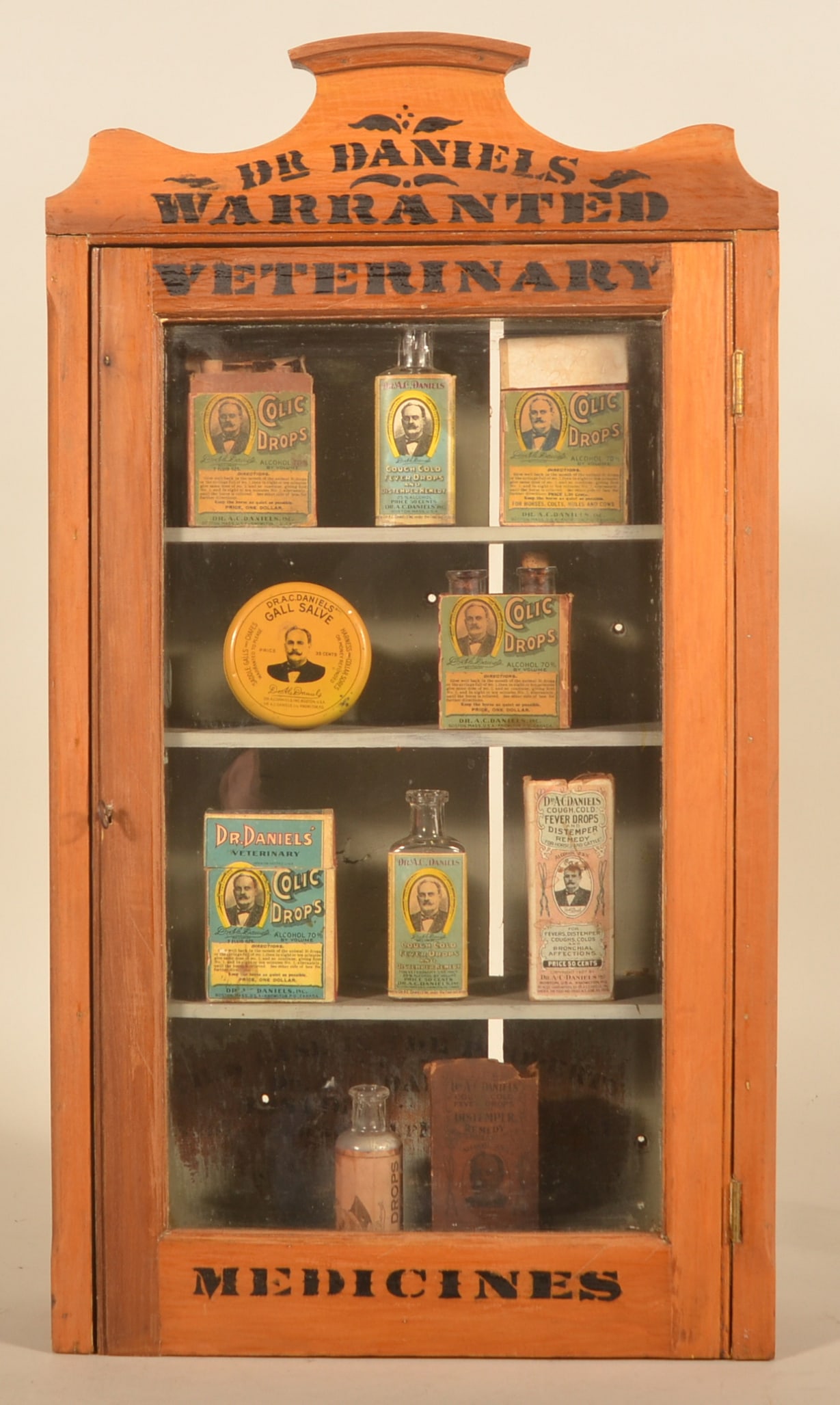 Dr. Daniels' Glass Front Veterinary Cabinet: 1st generation cabinet, ca. 1890-1900, predates the tin front cabinets which are more prolific. Excellent dry finish with remnants of the original varnish and strong black stenciling that says "Dr.