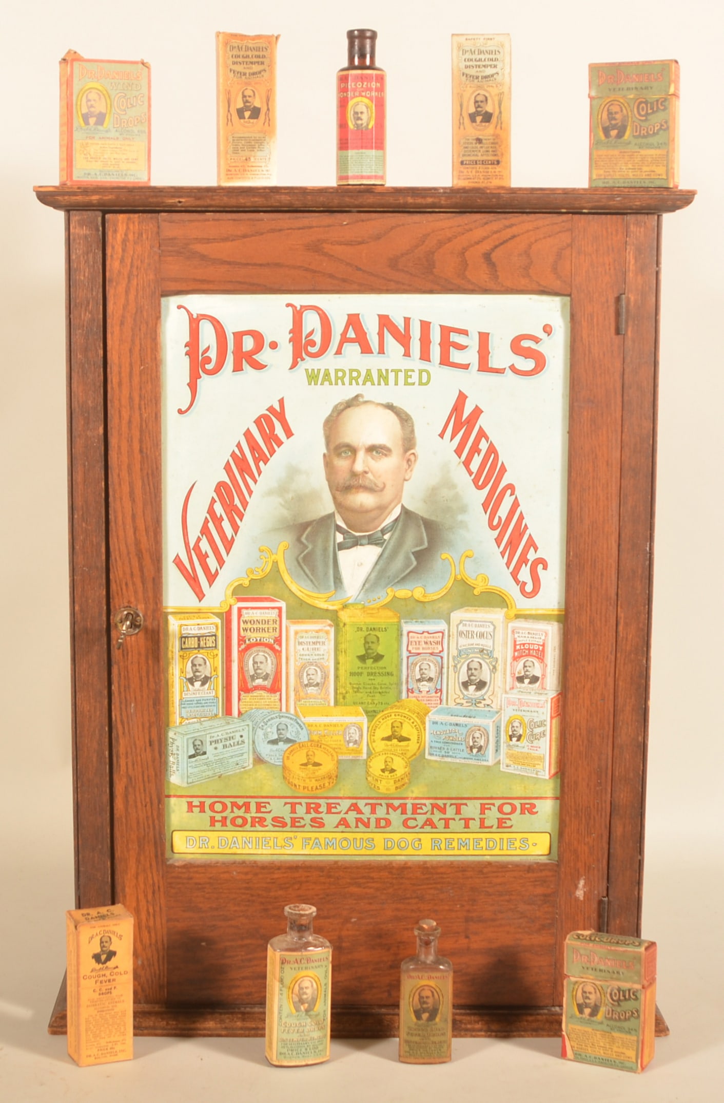 Dr. Daniels' Tin-Front Veterinary Cabinet: Iconic Dr. Daniels' embossed tin-front cabinet featuring a bust view with imagery of the many products produced by the company. The oak cabinet is in the original finish and has a warm patina from yea