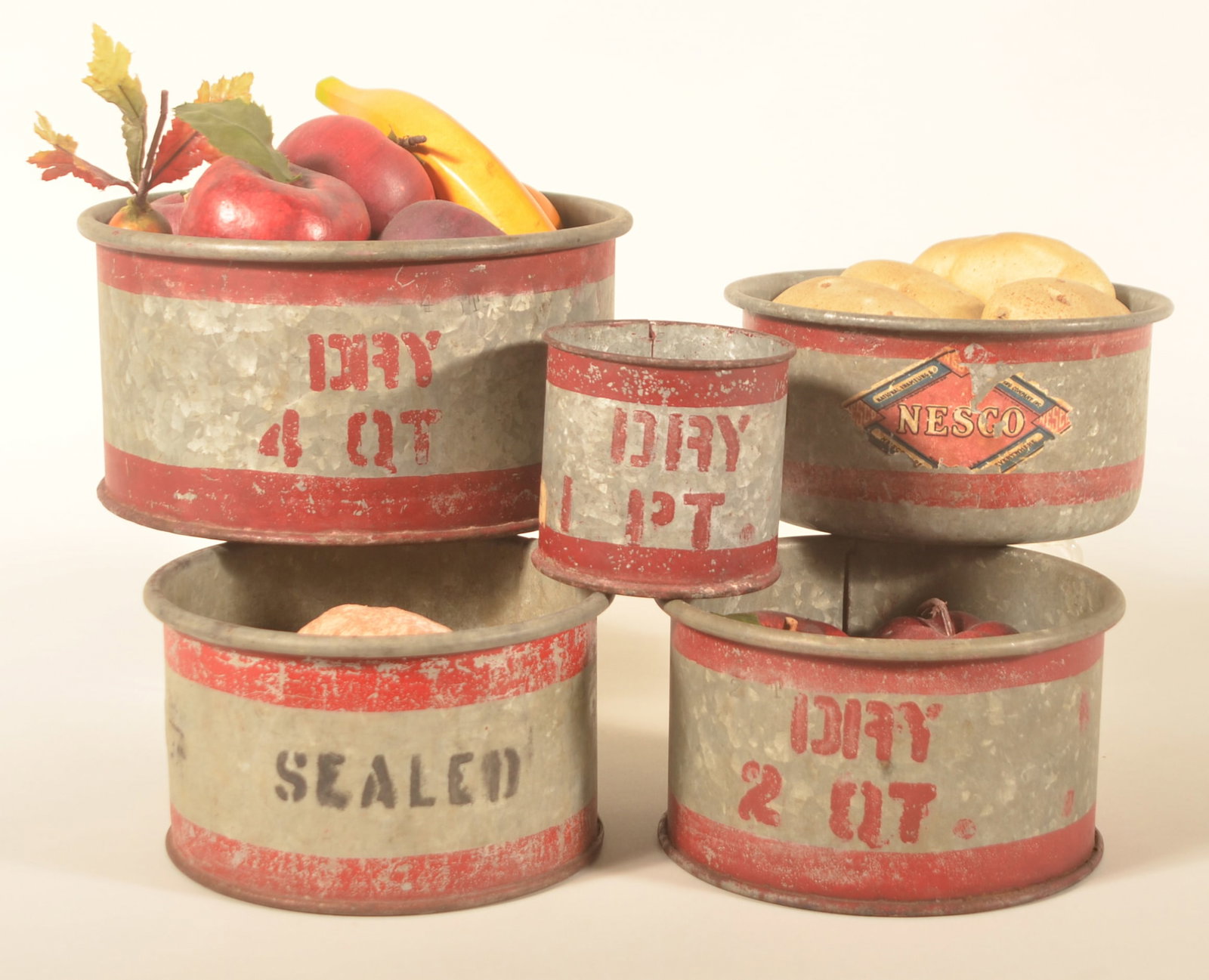 Five Different Zinc Red Stripe Dry Measures: 1-pint, two 2-quart, 4-quart, and a small round measure with original labels on each side. Several with display fruit. Provenance: The collection of Linda and the late Ed Althouse. Tallest, 4 3/4"H