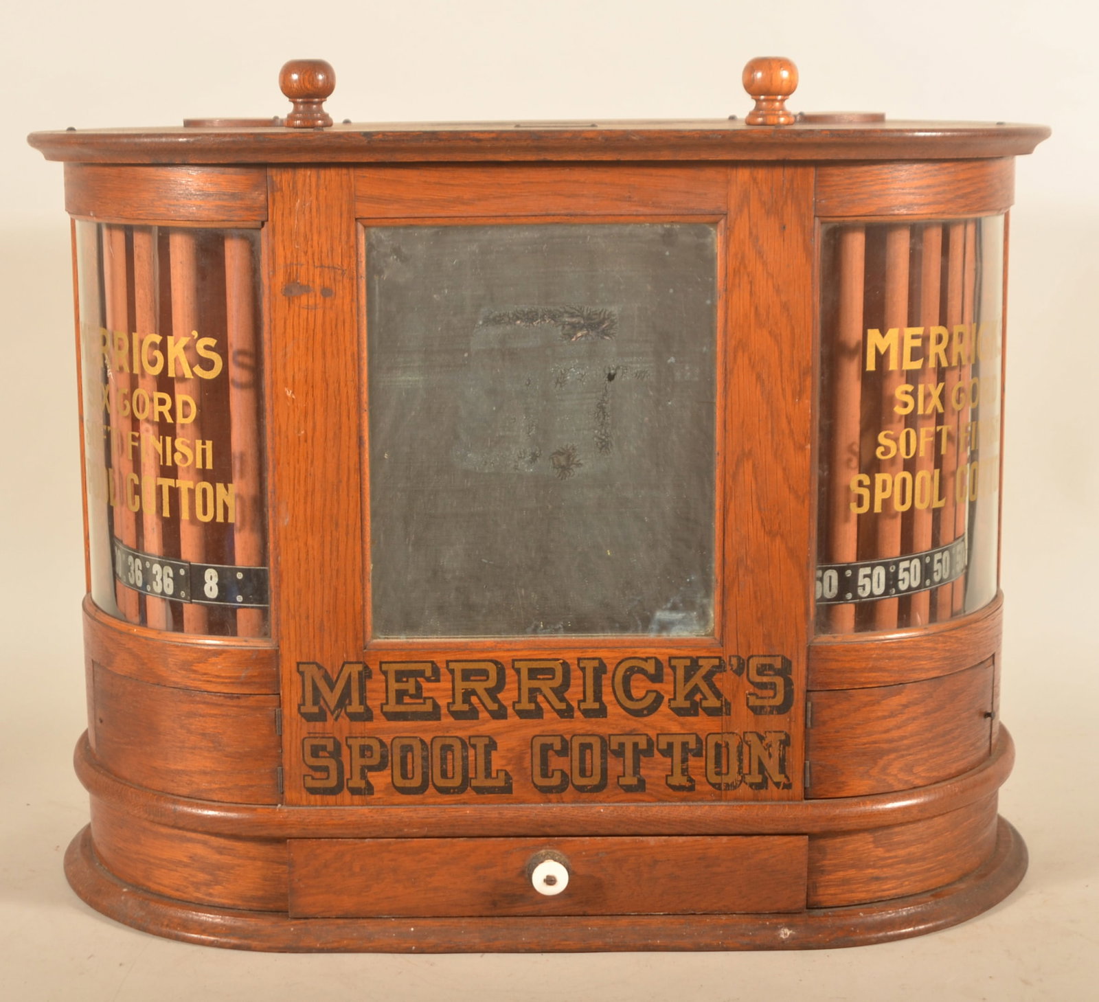 Excellent Oval Merrick's Spool Cotton Display Case: Beautiful cabinet in all-original condition. More difficult to find oval oak cabinet with mirrors in the center, glass ends which display the rotating spool holders. Small radiused doors open to allow