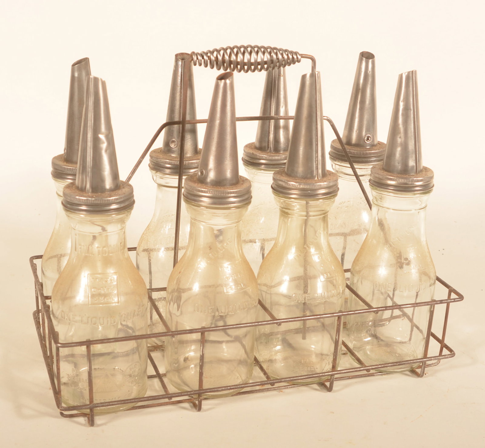Oil Bottle Carrier w/ 8 Matching 1-Quart Bottles: Mid-20th-century wire bottle carrier with matching oil bottles marked "64 MINN" inside a triangle along with other embossing. Provenance: The collection of Russell and Darlene Snyder. Carrier, 15"H x
