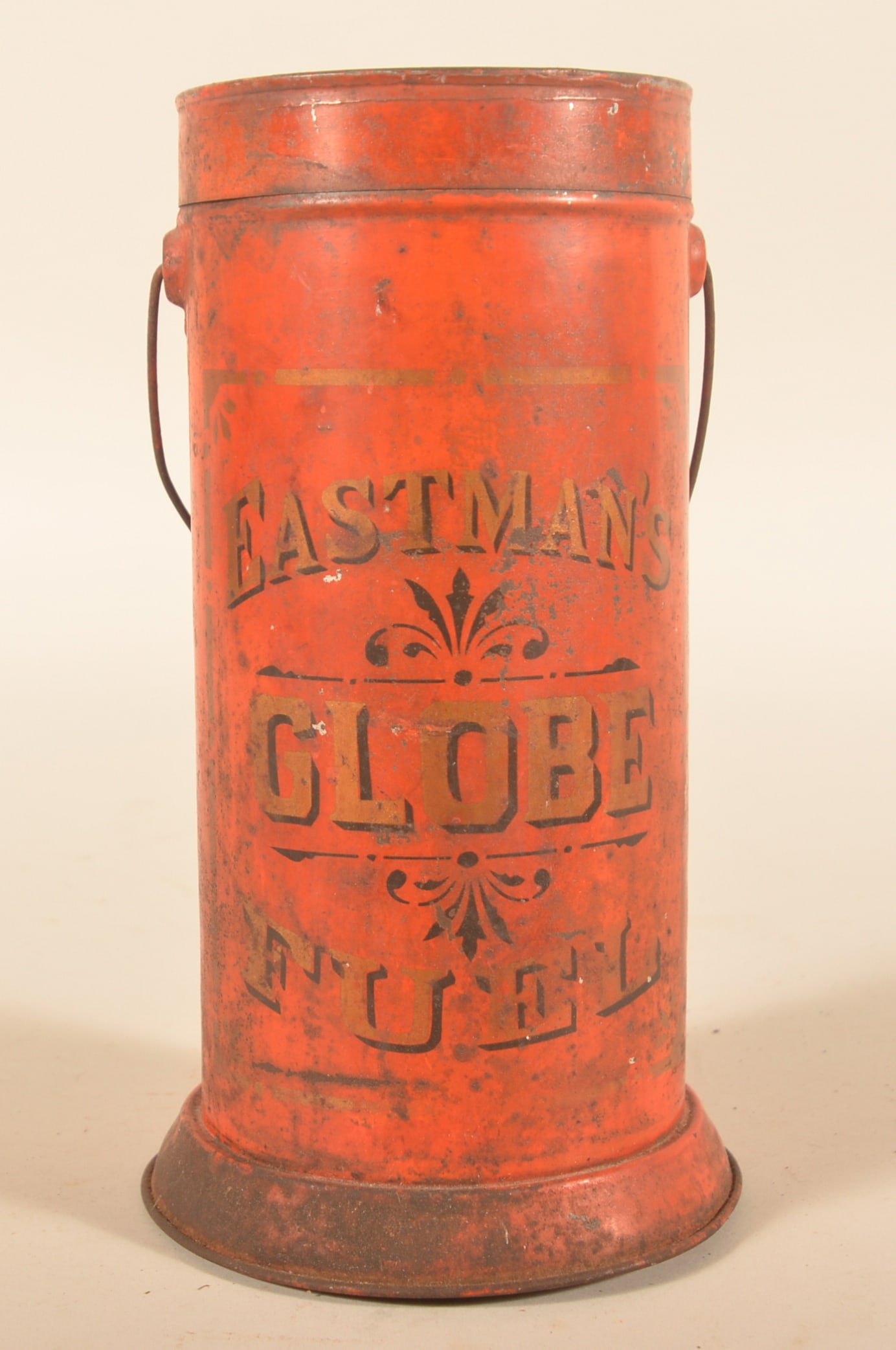 Early Lithographed Tin Eastman's Globe Fuel Can: Bail-handled tin with early lithographed graphics. Inside is a cast iron torpedo-shaped object with holes. Provenance: The collection of Russell and Darlene Snyder. 10"H x 5"D