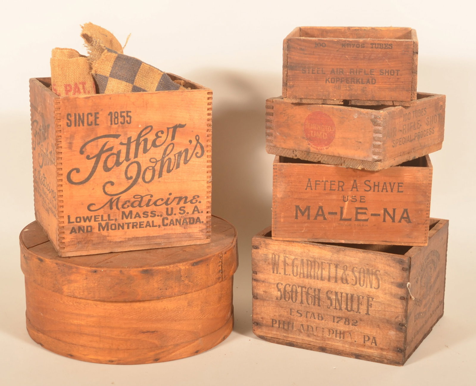 Group Antique Wood Shipping Crates: Five square crates including one stenciled "Father John's Medicine" and another stamped "W.E.Garrett & Sons Scotch Snuff". Together with a round cheese box and two burlap feed sacks. Provenance: The c