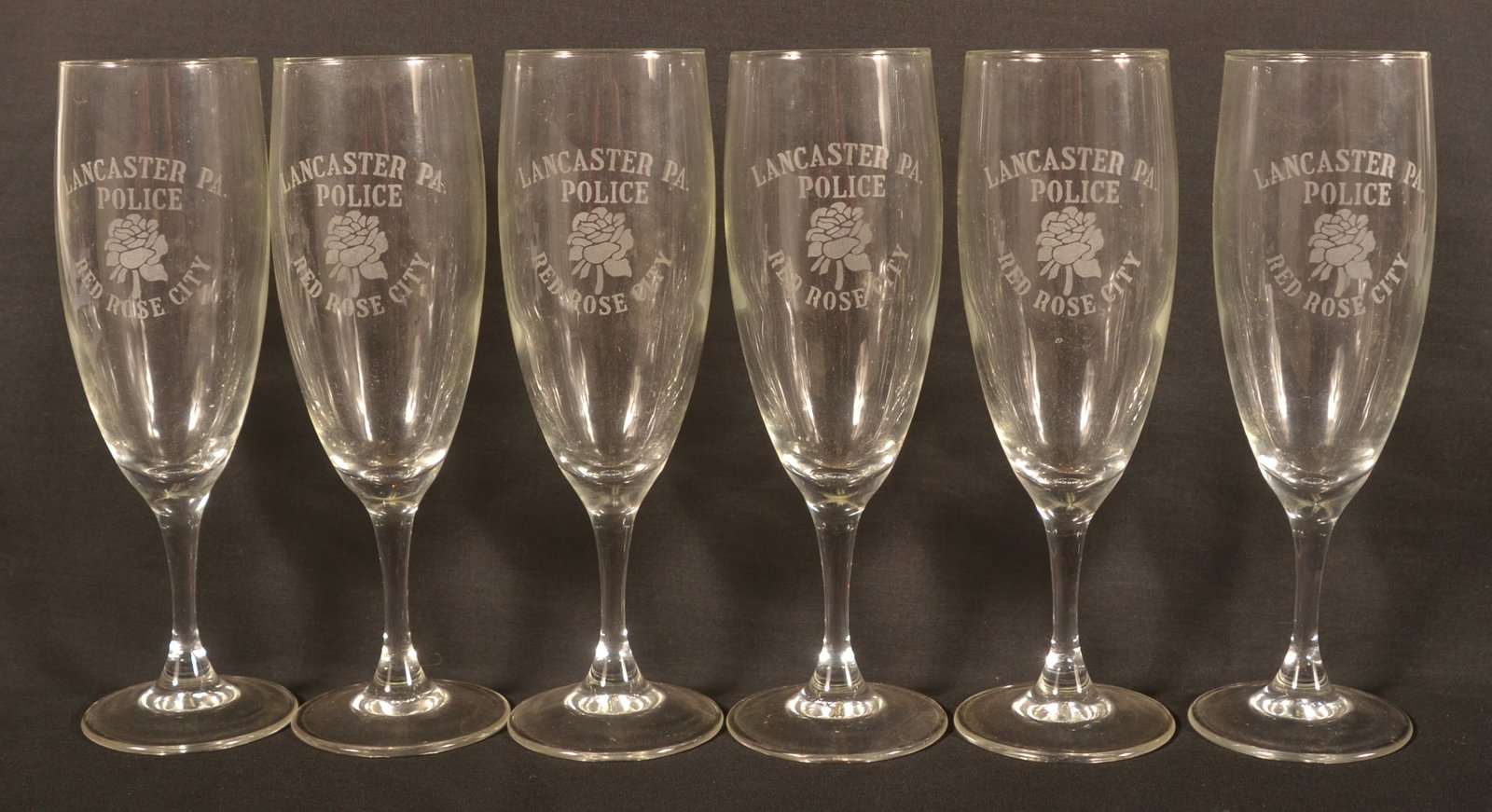 Set of 6 Flute Glasses Etched Lancaster, PA Police: Six glasses etched "Lancaster PA Police Red Rose City" with an etching of a rose. 6 7/8"H