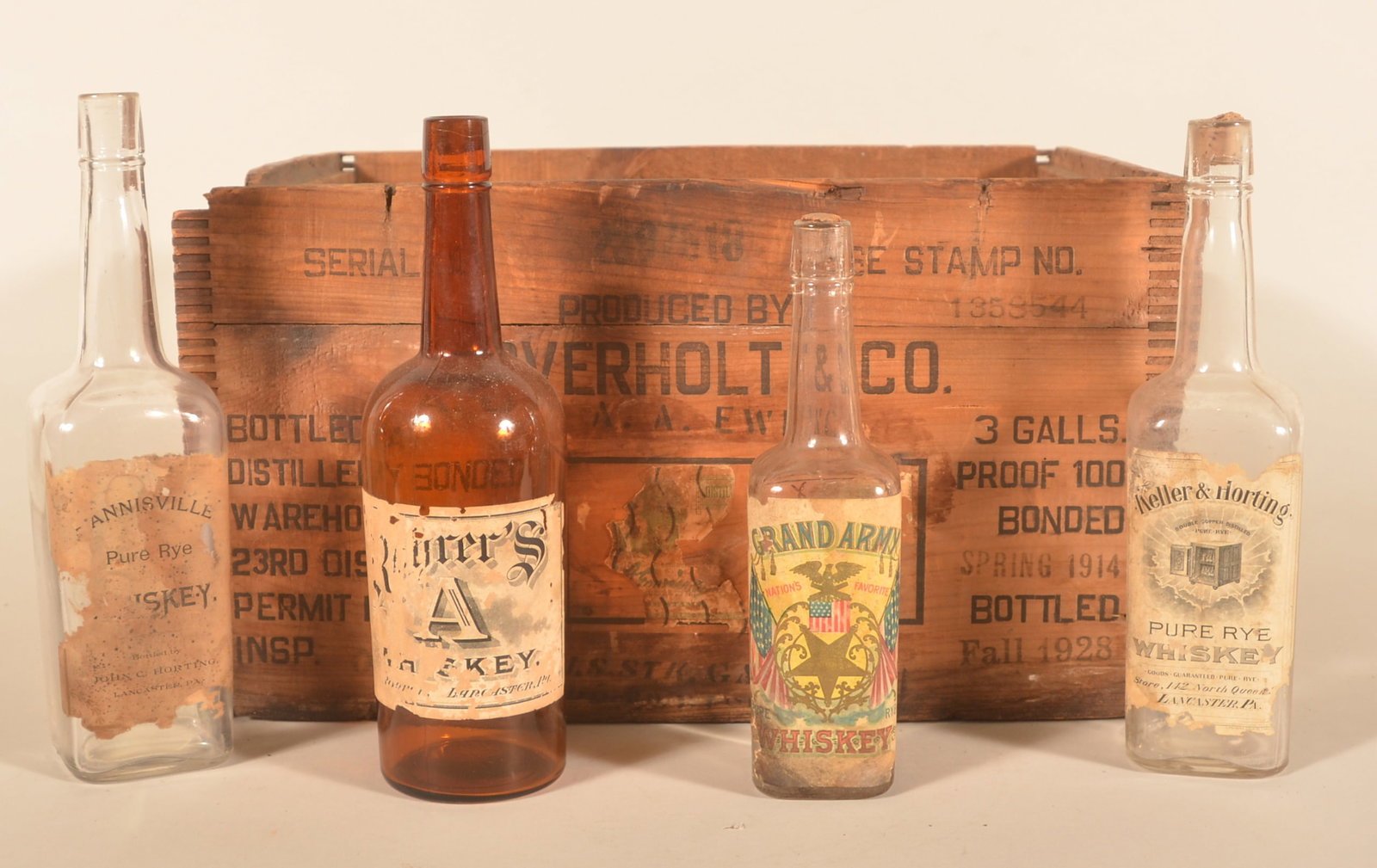 Paper Label Lancaster, PA Whiskey Bottles and Box: Four antique bottles including Rohrer's "A" whiskey, Hannisville Pure Rye by John Horting, Keller & Horting and a Grand Army Whiskey. Together with an "A. Overholt" bottled 1928 whiskey crate "For