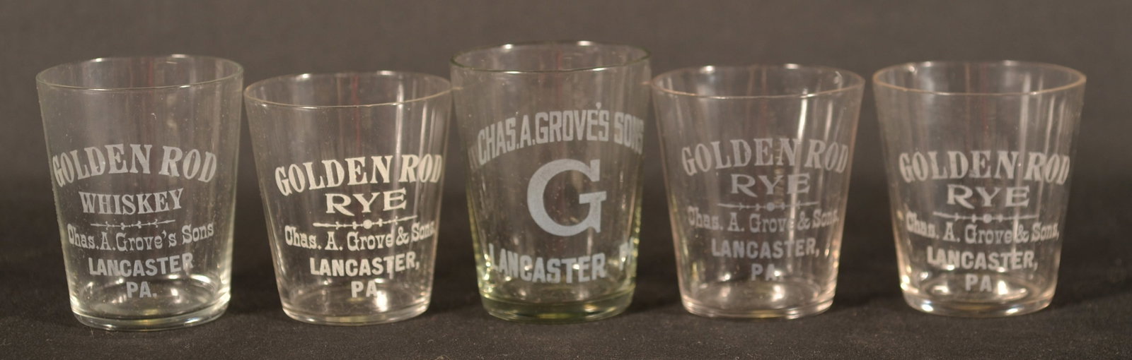Five Charles A. Grove Lancaster, PA Shot Glasses: Five sought-after shot glasses from a local distillery here in Lancaster, Pa. Four etched "Golden Rod Rye" and one etched "Chas A Grove's Sons" with a large "G". Tallest, 2 1/2"H