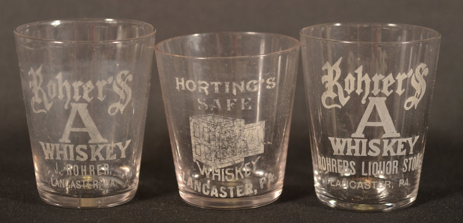 Rare Horting's Safe Whiskey & Rohrer Shot Glasses: Three shot glasses including two Rohrer's Whiskey glasses and a difficult-to-find Horting's Safe Whiskey glass which features an etched view of an open safe. 2 1/2"H