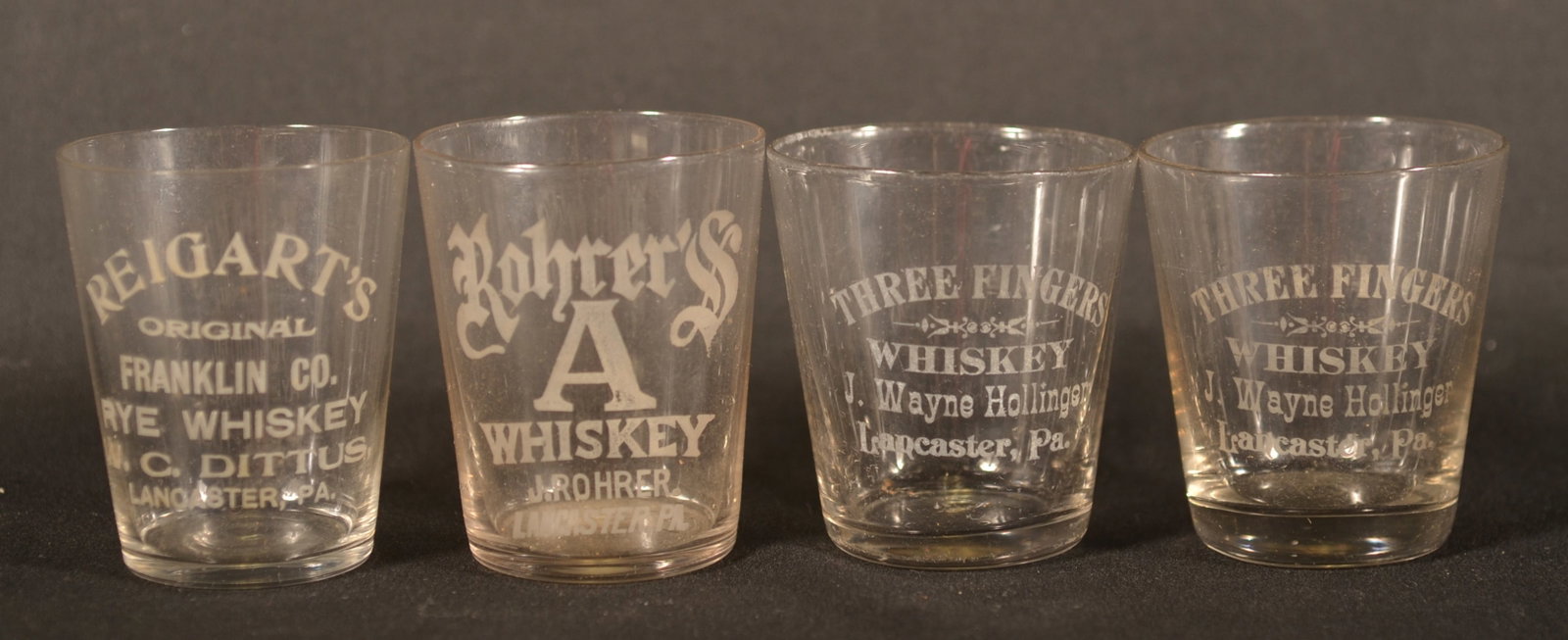 Four Lancaster, PA Etched Whiskey Shot Glasses: Rohrer's "A" whiskey, two rare Three Fingers Whiskey distilled by J. Wayne Hollinger and a Reigart's Franklin Co. Rye Whiskey. 2 1/4"H