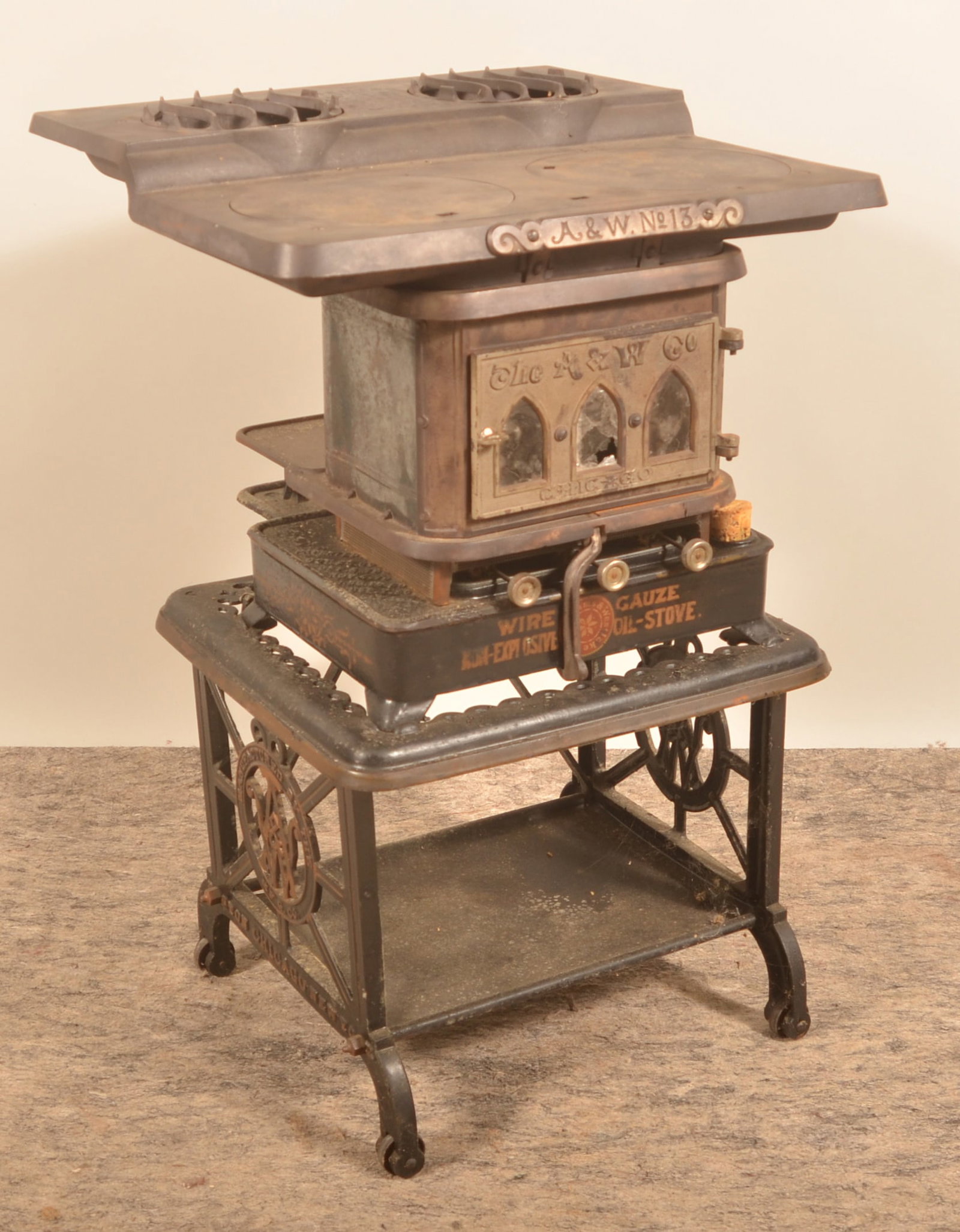 The A&W Chicago No.13 Wire Gauze Oil Stove: Small, portable oil stove with patent dates from 1881 to 1884. 3-burner stove with embossing and labelling on the cast iron. Shelf below for frying pans and utensils. Provenance: The collection of