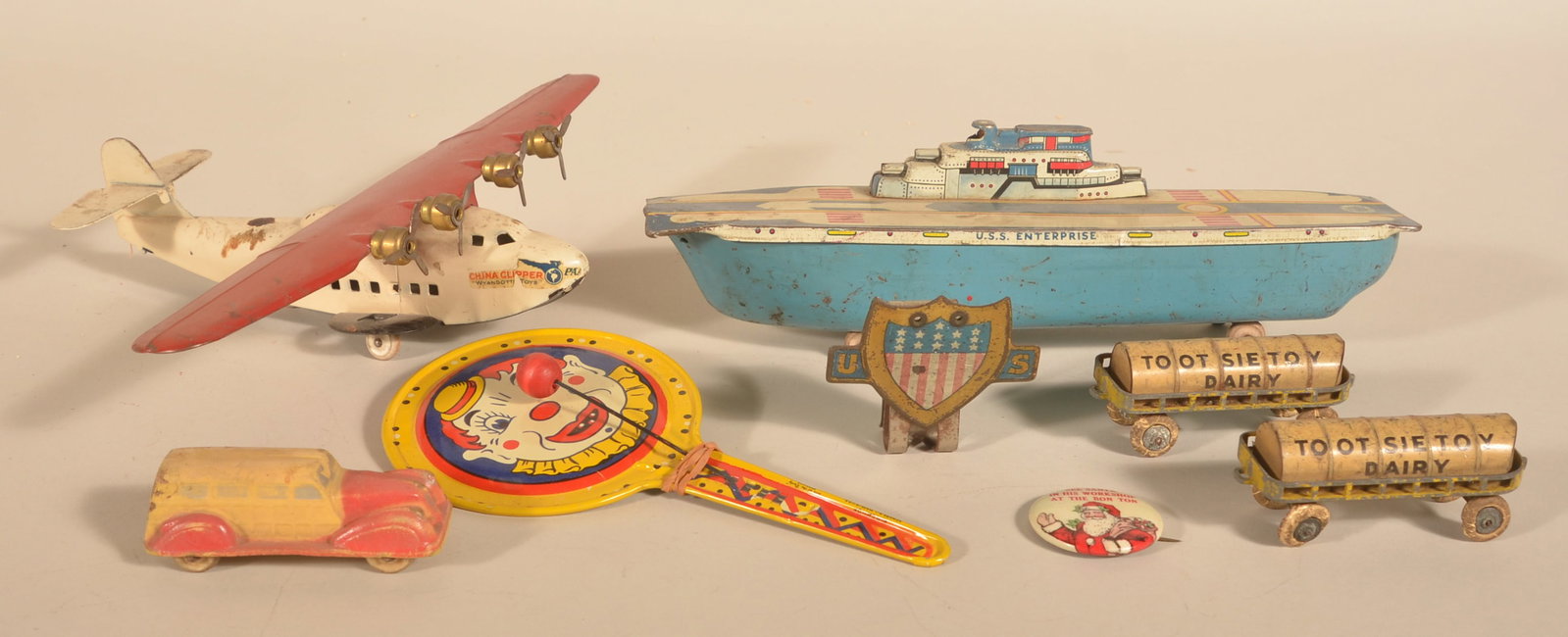 Wyandotte Pressed Steel Clipper Plane & Other Toys: Wyandotte airplane with labels on both sides of the nose. Two Tootsie Toy Dairy tanker cars, US patriotic shield that goes on a bike, composition station wagon, tin hand clapper, tin aircraft carrier 