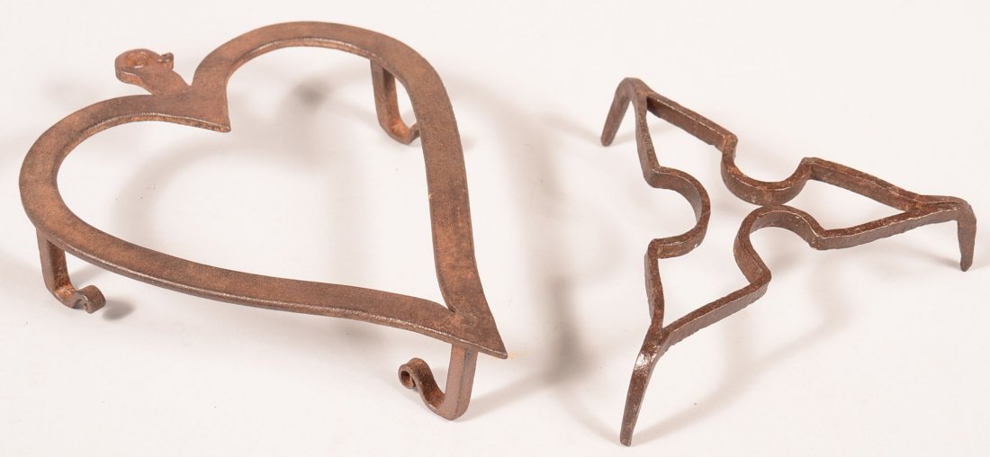 639. Two Iron Trivets. Including Heart shape trivet: 639. Two Iron Trivets. Including Heart shape trivet with tri-legs and feet with curled terminals, 1-3/4"h.x 10"x7-1/2", Triangular shape trivet, 2"h. Condition: Good.