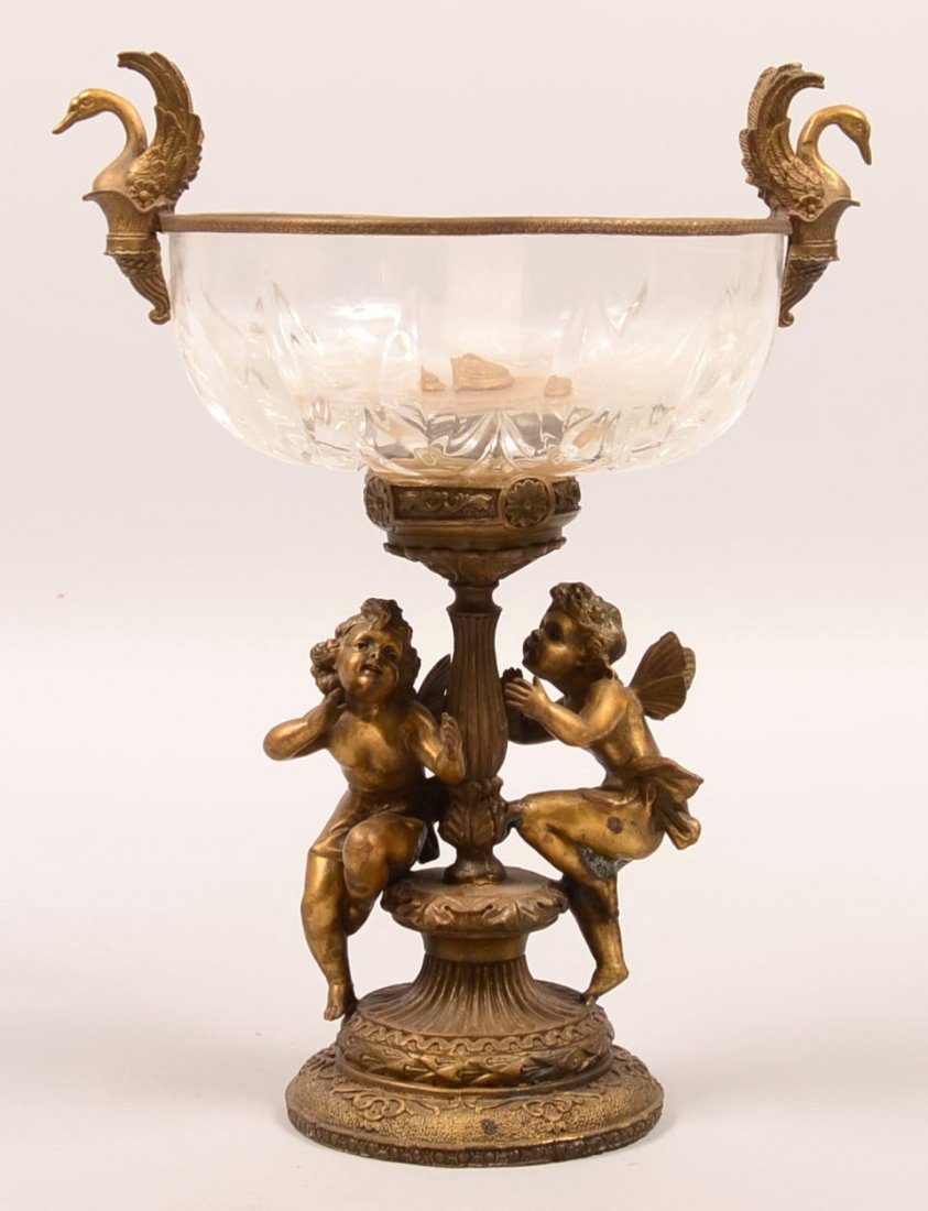 717. Brass Cherub Pedestal Console Bowl. Glass bowl: 717. Brass Cherub Pedestal Console Bowl. Glass bowl with brass rim collar having swan handles, double cherub on pedestal base,14-1/2"h. Condition: Good.