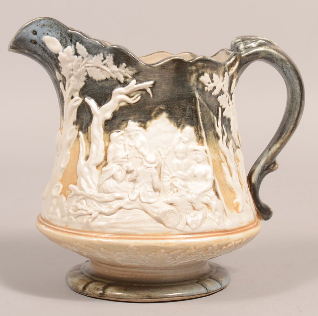 802. Tan and Green Salt Glazed Earthenware Pitcher with: 802. Tan and Green Salt Glazed Earthenware Pitcher with Embossed Camping Scene. Stamped on base "MADE IN ENGLAND". 8"h. Condition: Very good.