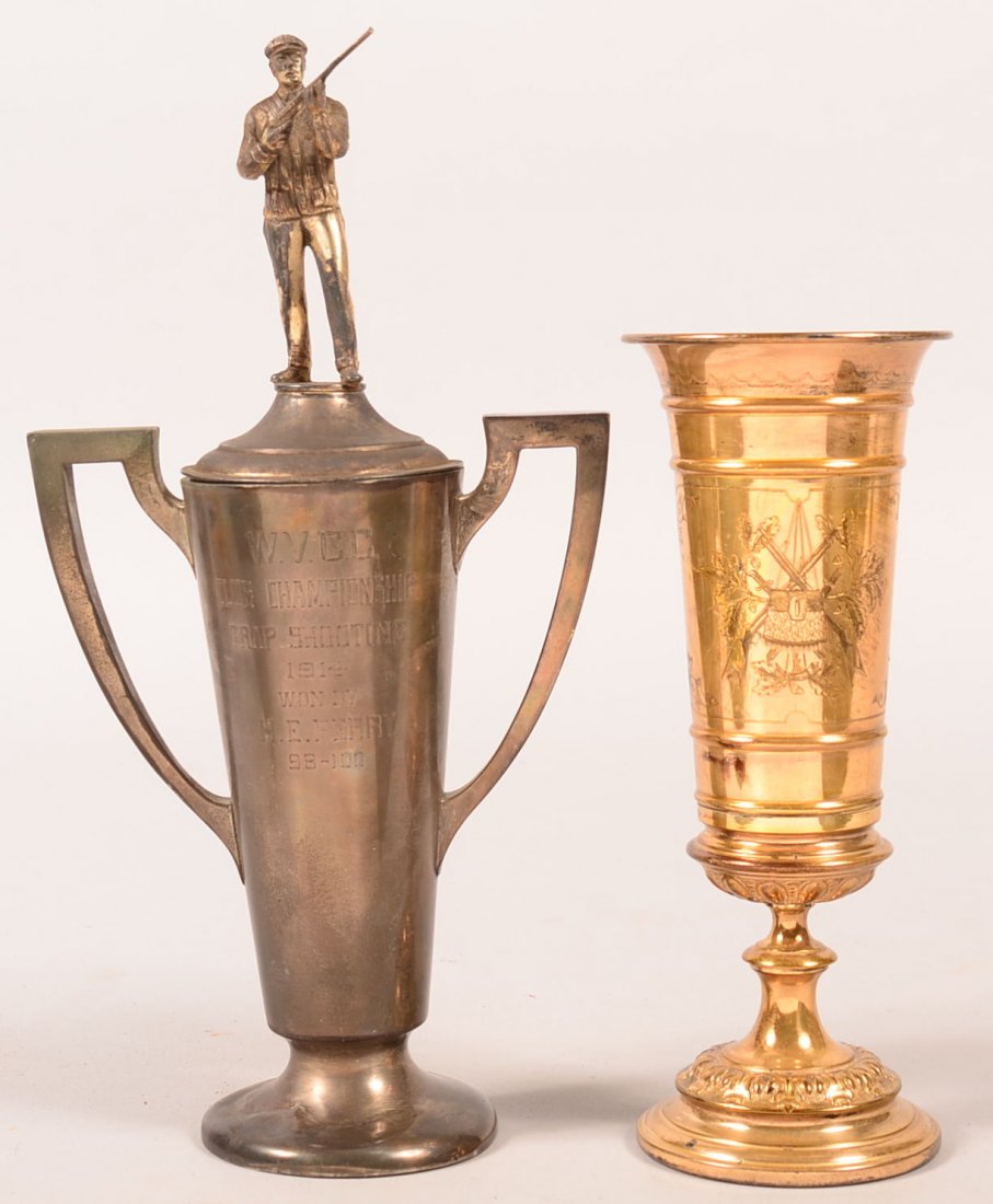 Lot of (2) shooting trophy cups. The first is brass: Lot of (2) shooting trophy cups. The first is brass 9-1/2" tall engraved on one side showing crossed musket and crossbow behind a target and on the other side crossed Scheutzen rifles. The second has 