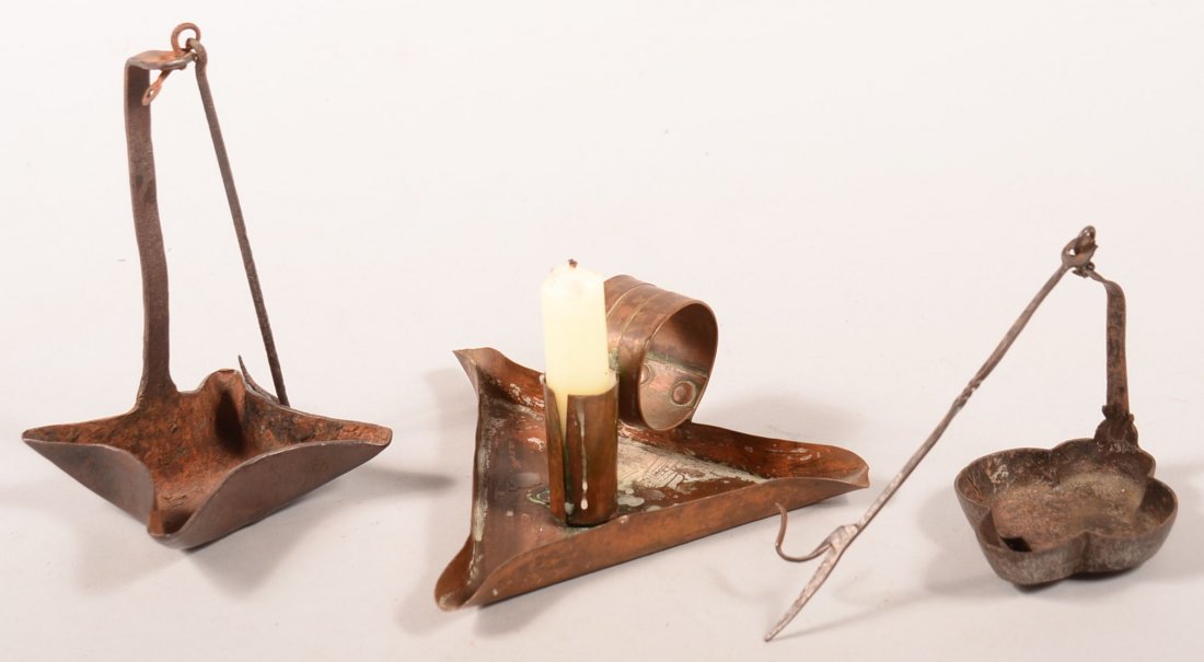 Three Lighting Devices. First is a iron four wick open: Three Lighting Devices. First is a iron four wick open betty lamp style lamp with hanging hook, 6-1/2"h. Second is a Copper three wick open pan and candle holder lamp with applied handle, 2-3/4"h. Thi