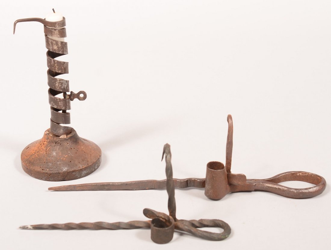 Three Iron Lighting Devices. Iron spiral Candlestick: Three Iron Lighting Devices. Iron spiral Candlestick with wooden base, 7"h. Two wrought iron Miner's sticking tommy candle holders, 8-1/4" and 12"l. Condition: Good with losses on wooden base.