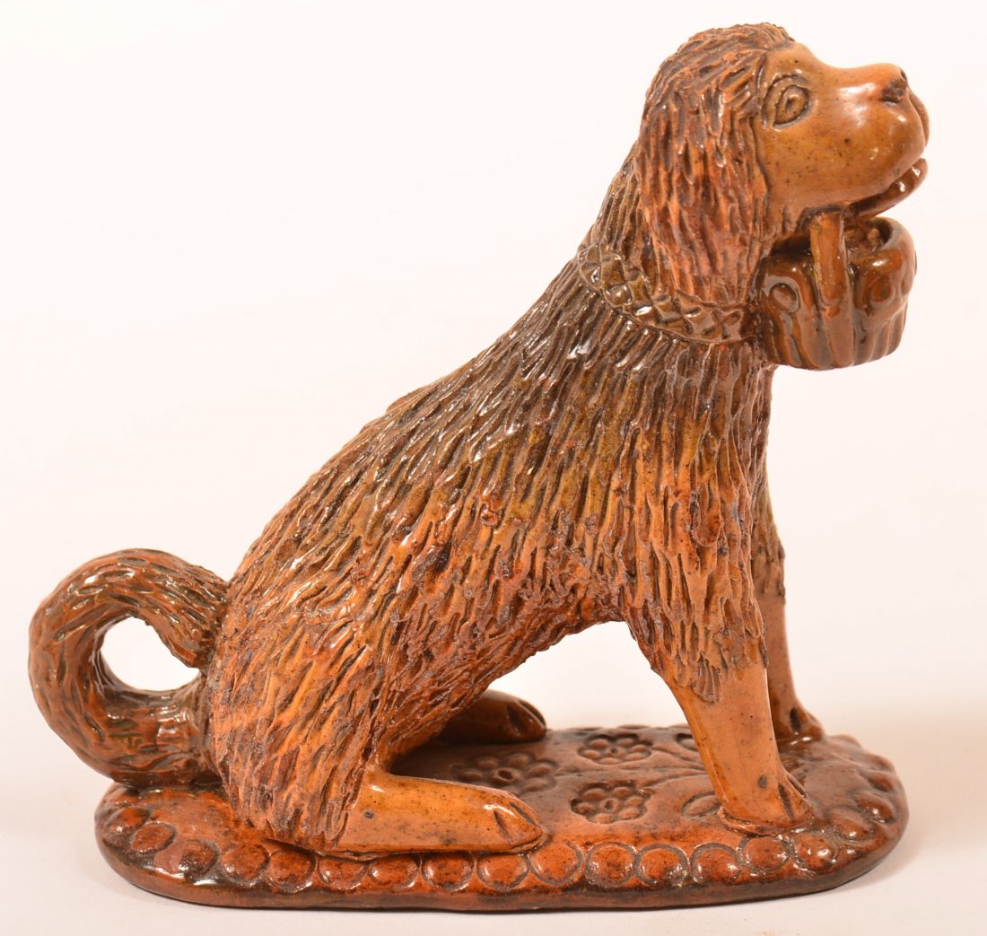 Redware Figure of a Seated Dog.: Redware Pottery Hand Modeled Figure of a Seated Dog with Basket in Mouth, attributed to Bell Pottery. Mounted on an oval slab base with interior rattle. 5"h. Condition: Good, professional repairs to b