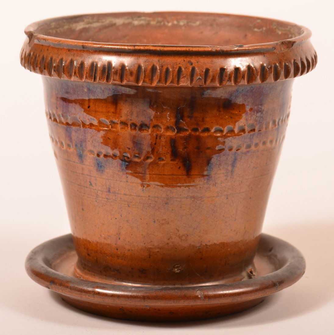 Mottle Glazed Redware Flower Pot.: Mottle Glazed Redware Flower Pot with Attached Saucer Base. Molded rim with tooled edge, double coggle wheel incised band on tapered body.5-3/4"h. x 6" diam. Condition: Good, three chips on upper rim.