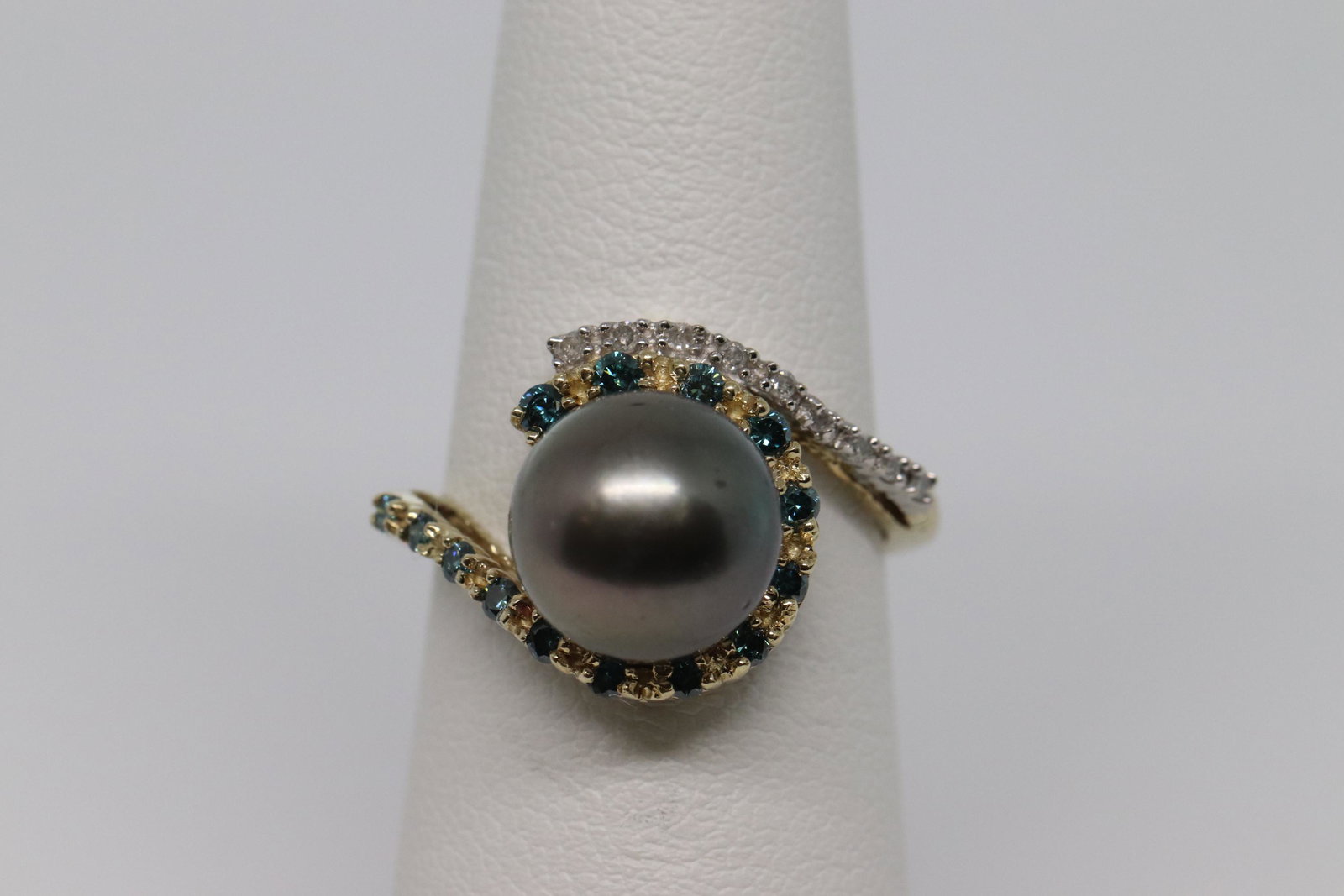 14kt Diamond & Pearl Ring: A ladies 14kt Yellow Gold Diamond Ring with Round Black Pearl in the center and Blue and White Diamonds around the Pearl stone in the center. There are a total of 23 Round Brilliant diamonds. The ring
