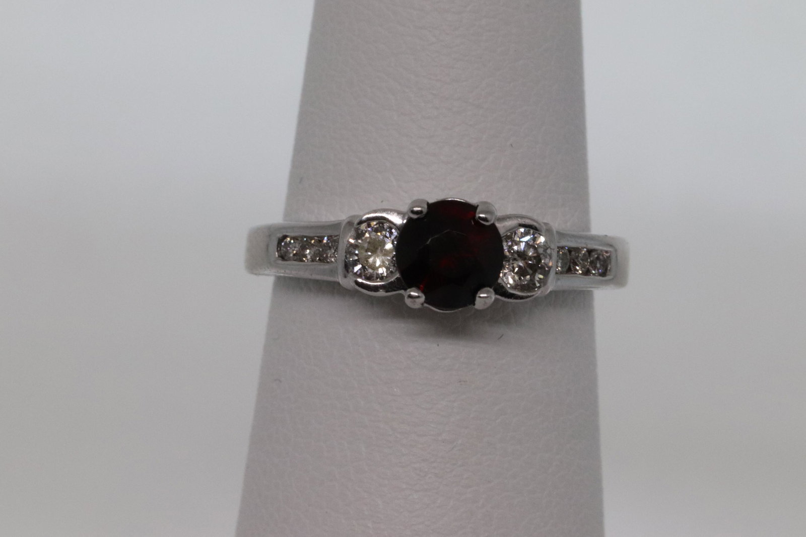 14Kt Diamond & Garnet ring: A 14kt White Gold Diamod Ring. The ring has 8 round brilliant diamonds on the side and a Dark Red Garnet Stone on the center. Diamonds weight: approx 0.20tcw. Garnet measures 5.50x5.46mm. Ring size 5.