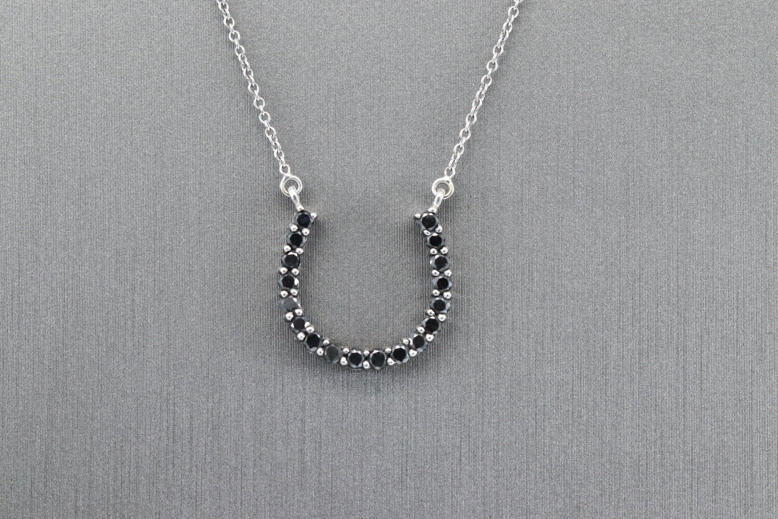 14kt Black Diamond Horse Shoe Necklace: A ladies 14kt white Gold Black Diamond Necklace. The pendant is a horse shoe design. 18 round black diamonds set on the pendant. Total length is about 22in. Total weight is 2.90gr.