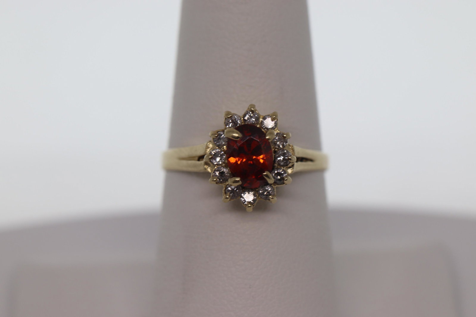 14Kt Yellow Gold Ladies Diamond & Garnet Ring: A ladies 14kt Yellow Gold Diamond ring with a Garnet stone in the center. The Garnet stones color is orange color. There are a total of 12 round brilliant diamonds set around the center stone. The rin