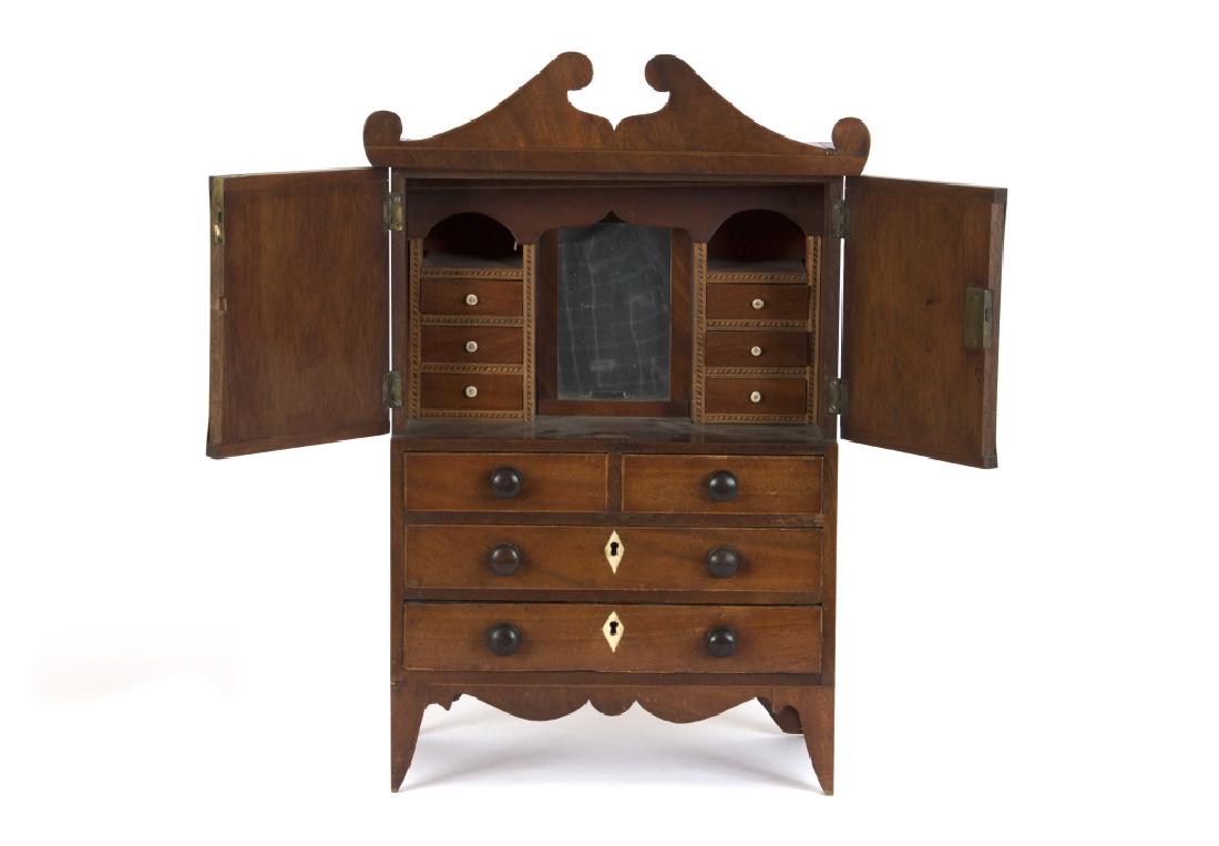 An inlaid fruitwood jewelry case: Mid 19th c. In the form of a miniature Chippendale cabinet. With mirrored fitted interior. 22" H x 13" W x 7" L. Condition: minor chip to edges and cornice. (GMP 29)