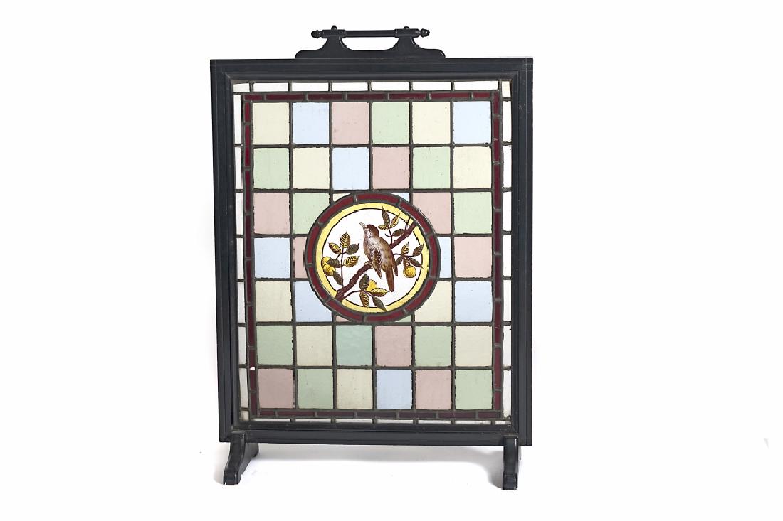 A Victorian leaded glass fire screen: The multi colored square panels centered with a circular image of a bird in a fruit tree, all within an ebonized wood frame. 31in. H x 9in. W x 22in. L Condition: one square panel with slight hairline