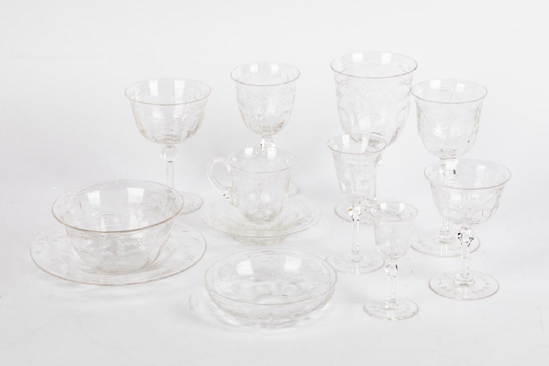 A Thomas Webb suite of cut glass tableware: Early 20th century. Each signed and with etched foliate and floral garlands. Includes 12 cups and 12 saucers, 14 finger bowls, 8 shallow bowls, 13 small plates, 11 cordials, 12 sherry, 12 goblets, 12