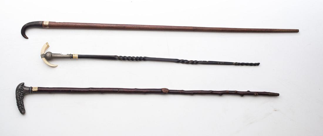 A group of three walking sticks: One blackthorn shillelagh form topped with a cast antler form handle, 26 1/2in. L. The second of zitan wood with a horn handle, 28 1/2in. L. The third of ebonized hardwood caved with spiral twis