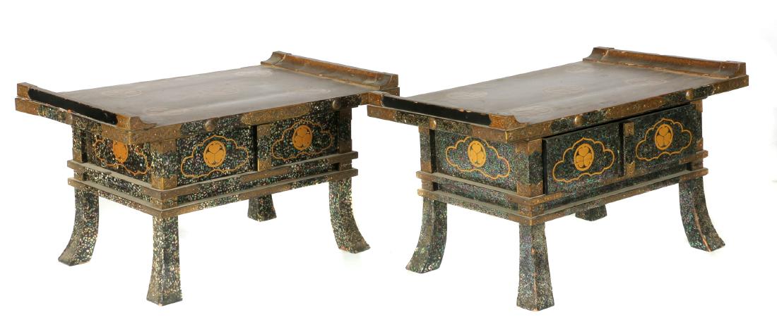 A pair of Japanese gilt lacquer offering stands: Meiji period Raised on four splayed feet fitted with etched copper housingsThe gilt decorated top with scrolled terminals set above a waisted section revealing a drawer, displaying a mother-of-pearl i
