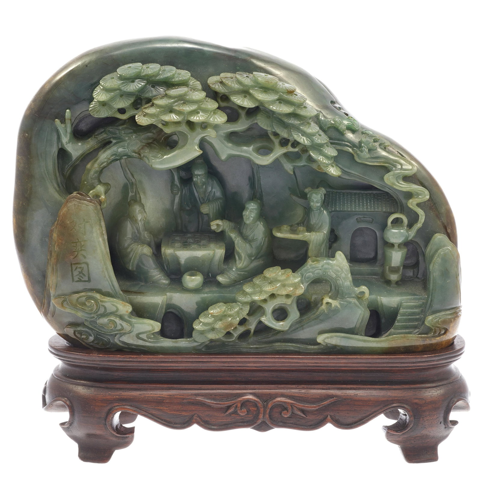 A green jade boulder carving, 20th century: Carved with a group of three scholars, two playing chess while the other watches, all beneath overhanging rocks within a pine grove, the reverse featuring a wandering scholar, wood stand. Width: 7in.