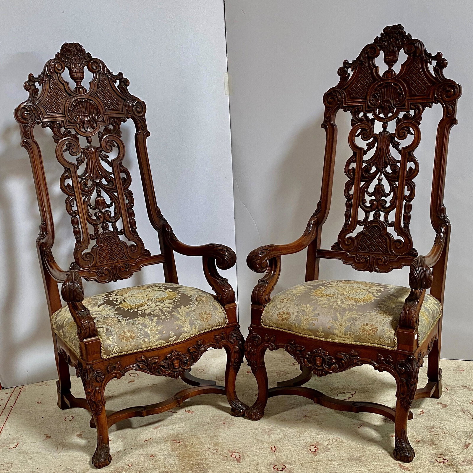Pair Flemish Baroque Style Armchairs: First Quarter 20th Century. Each with an arched crest carved with a floral filled urn over a back panel carved with lattice panels, acanthus scrolls and bell flowers raised on cabriole legs ending in 