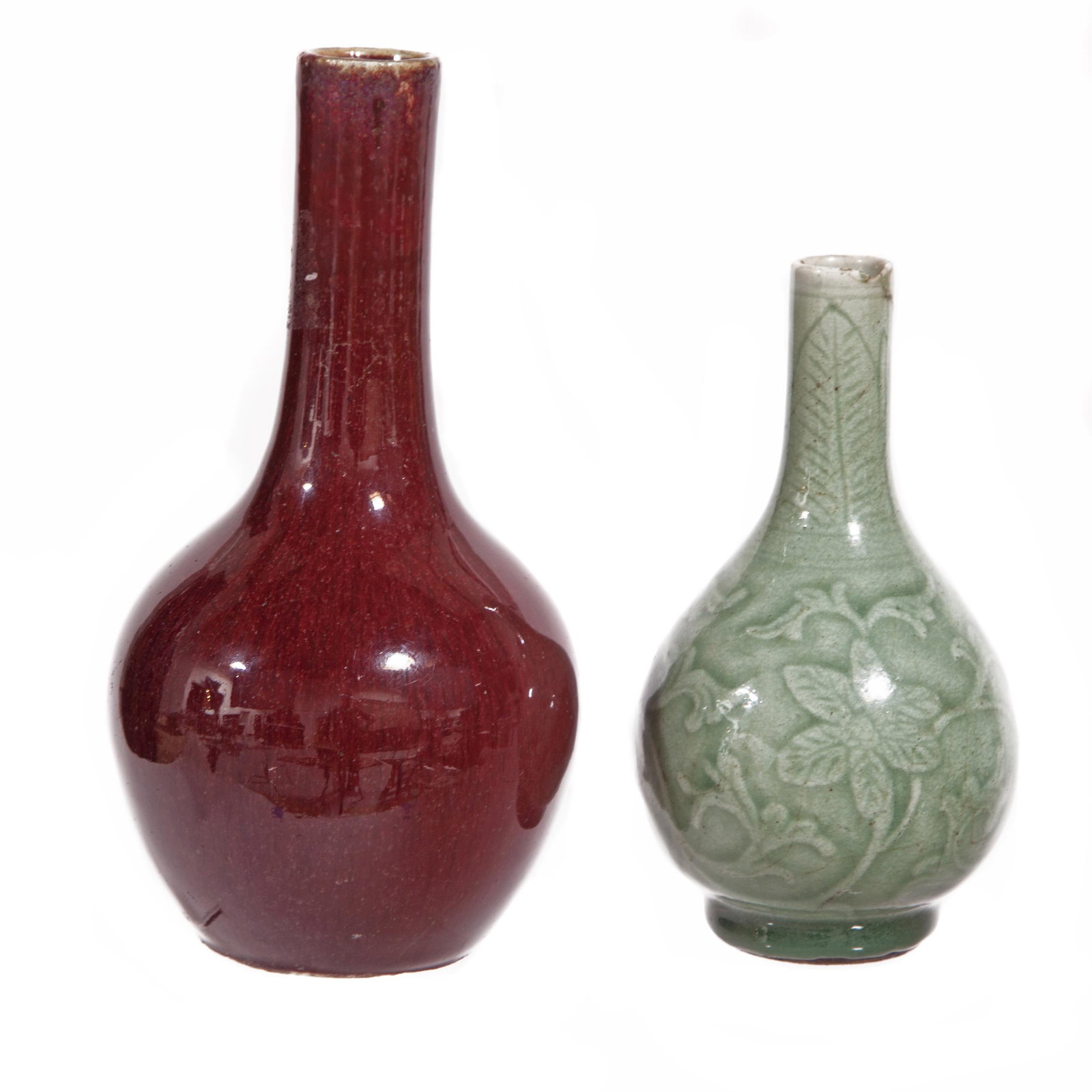 Two Glazed Bottle Vases, Ming Dynasty and Later: Comprising a celadon glazed vase with carved decoration of floral scrolls, and a flambe glazed vase with an overall oxblood red hue. Height: 6 1/4 and 8 inches Condition: The celadon vase has a rest