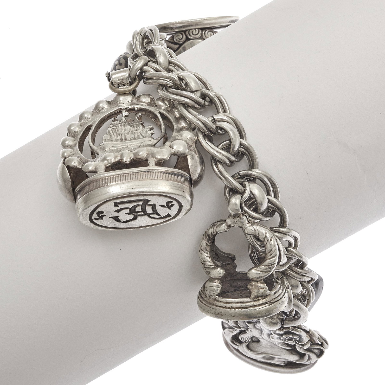 Sterling Silver Multi- Fob Charm Bracelet: The sterling silver double cable link chain suspending six fobs: one sterling silver scrolled seal, "ES"; one sterling silver hinged claw-shape fob; one sterling silver ship with seal "FDC", one sterl