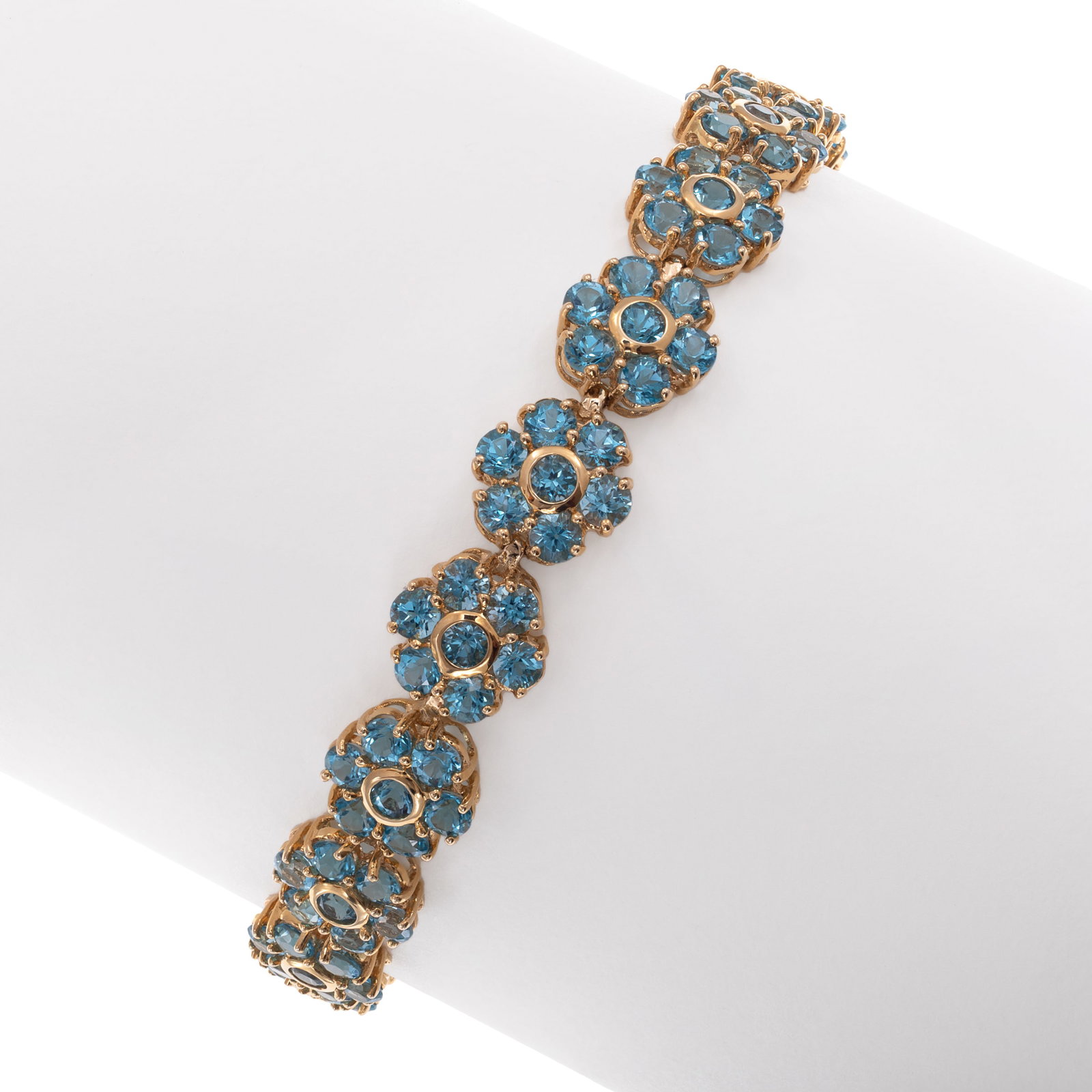 Blue Topaz, 14k Yellow Gold Bracelet: Blue Topaz, 14k Yellow Gold Bracelet Designed as a series of nineteen flowers, each accented by seven round-cut blue topaz weighing a total of approximately 15.95 cttw., set in an articulated, 14k