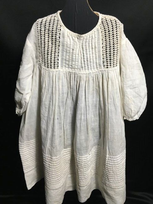 Antique Doll Dress: Antique cotton dress with bottom pintucking and crocheted lace inserts. Dress would drape, not waist. Minor age imperfections. 19" long with a sleeve length of 7". Ships from Canada.