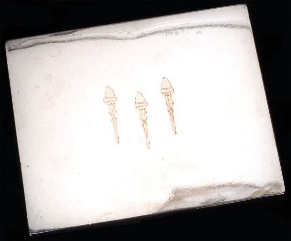 A CARTIER SIGNED STERLING SILVER PLAYING CARD BOX,: A CARTIER SIGNED STERLING SILVER PLAYING CARD BOX, the spring filled push-lever opens skillfully fitted lid to reveal divided interior, the lid inlaid with copper or rose gold torches. 5 3/4 in. by 4