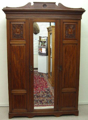 AN EDWARDIAN MAHOGANY THREE-DOOR ARMOIRE, English,: AN EDWARDIAN MAHOGANY THREE-DOOR ARMOIRE, English, c. 1905. The large wardrobe is divided into two vertical sections behind three full-length doors, the mirror-paneled door centered between carved woo