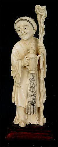 A CHINESE IVORY CARVED FIGURE of a woman standing,: A CHINESE IVORY CARVED FIGURE of a woman standing, holding a large staff in one hand, a covered tea pot in the other with scrimshawed decoration on robe hanging. Height 5 1/2 in., on attached wooden p